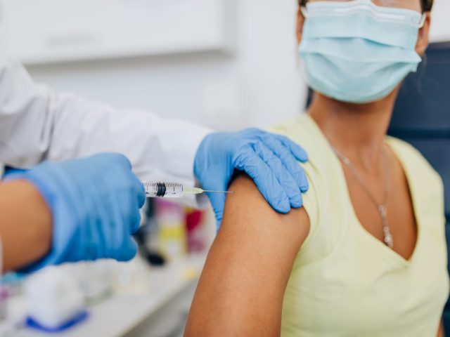 Female doctor or nurse giving COVID-19 vaccine to a patient's shoulder. Vaccination and prevention against virus pandemic. Photo of nurse giving patient COVID vaccine