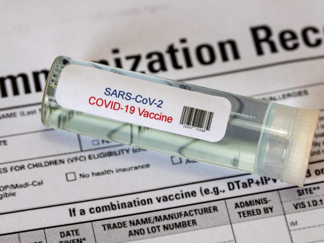 SARS-CoV-2 Covid-19 Vaccine on Immunization Record A vial of COVID vaccine laying on top of an immunization record