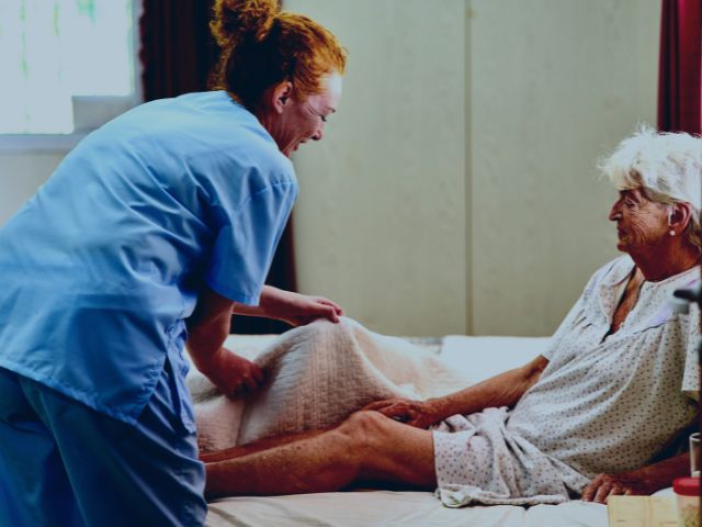 Nurse helping a home care patient who recovered from DVT into bed.