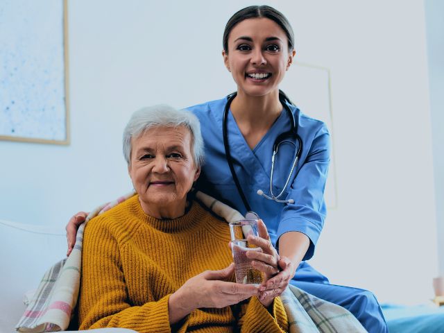 A geriatric nurse and her patient smiling and posing for a picture together.