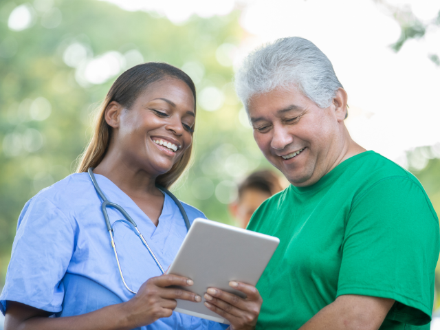 Nurse in blue scrubs talks with a man in a green shirt as part of a public health initiative, similar to what the U.S. surgeon general oversees.