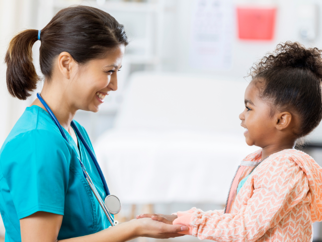 A pediatric nurse speaks to a young girl in a doctor's office, possibly about how to prevent bullying