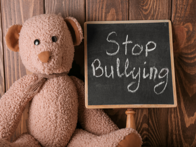 A brown teddy bear holds a chalkboard sign with the words,
