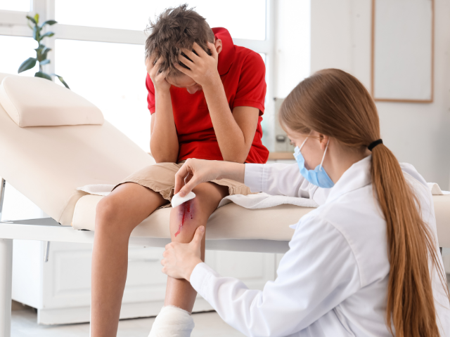 A doctor dresses a wound on a young boy's knee as part of pediatric wound care.