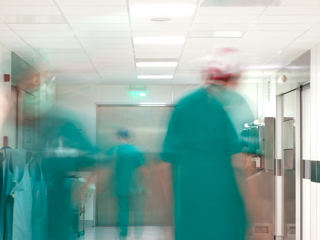 A busy hospital emergency room depicted as blurred nurses in teal scrubs running across the ER.