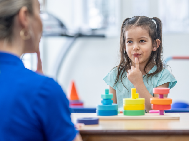A nurse sits across from a child who is playing with block toys as a form of play therapy
