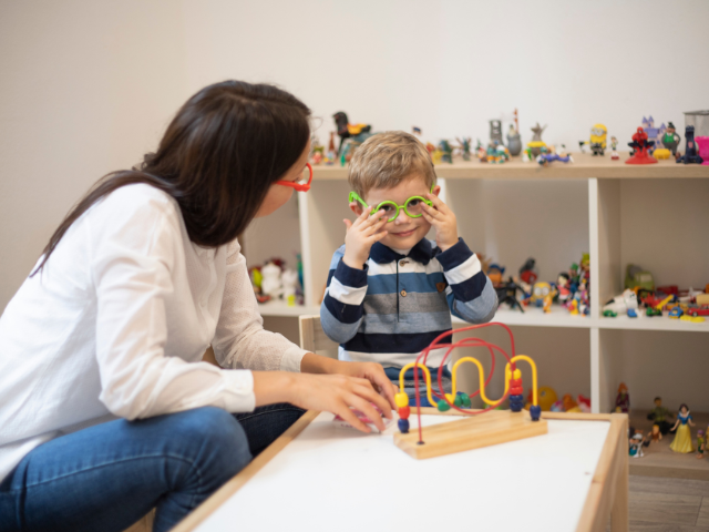 A nurse sits across from a child who is playing with toys as a form of play therapy