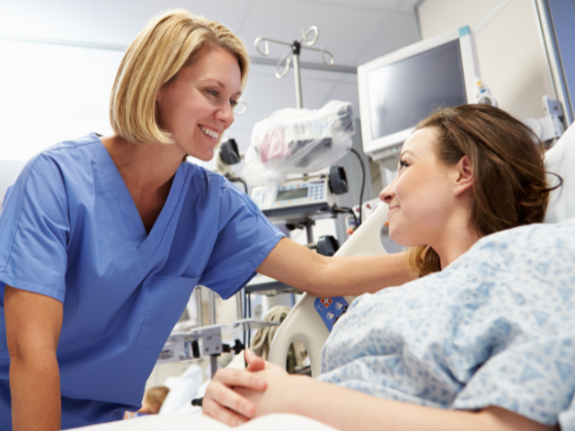 A nurse, who could have collective bargaining rights, speaks to a woman in a hospital bed.