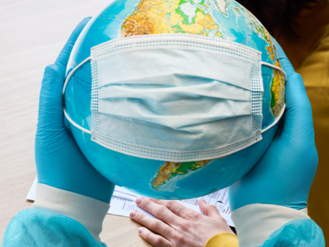 A medical professional wearing gloves holds a globe that has a face mask on it, representing infectious disease prevention.