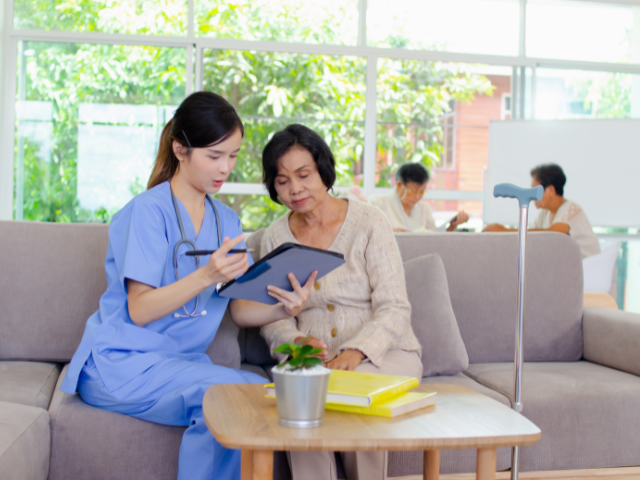 A nurse sits with a patient explaining information on a tablet.