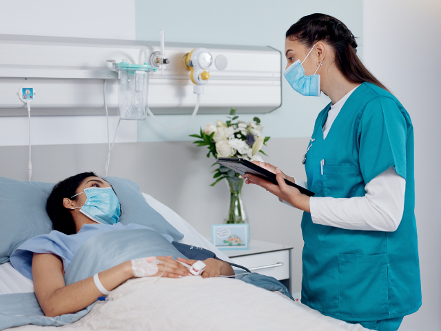 A nurse wearing a face mask checks on a patient who also is wearing a face mask.
