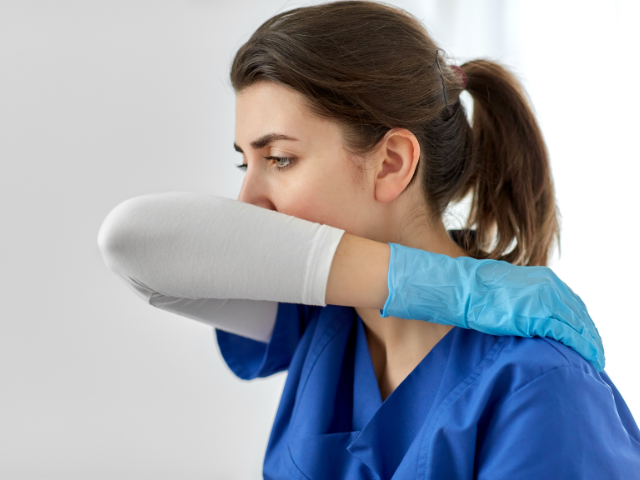 A nurse coughs into her elbow