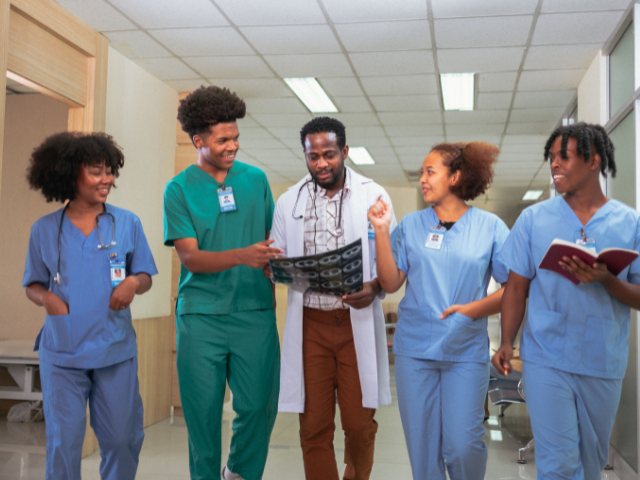 A group of nurses, with a doctor in the middle, walk down a hallway as they examine an X-ray.