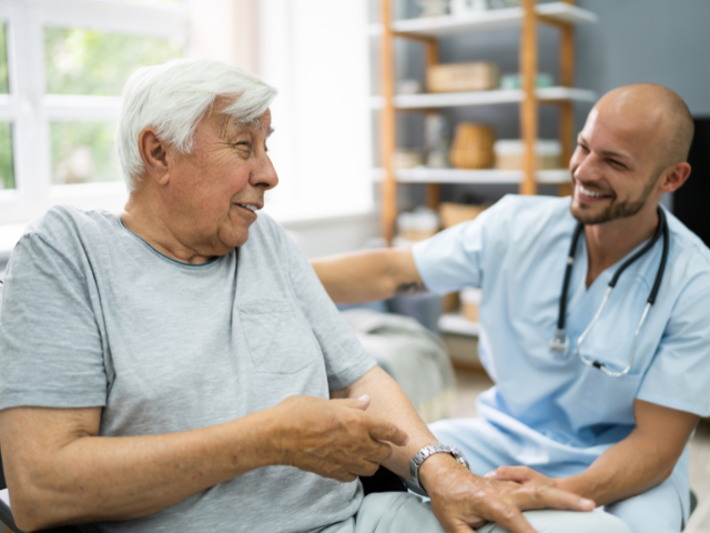 A male nurse sits down with a male patient and has a conversation.