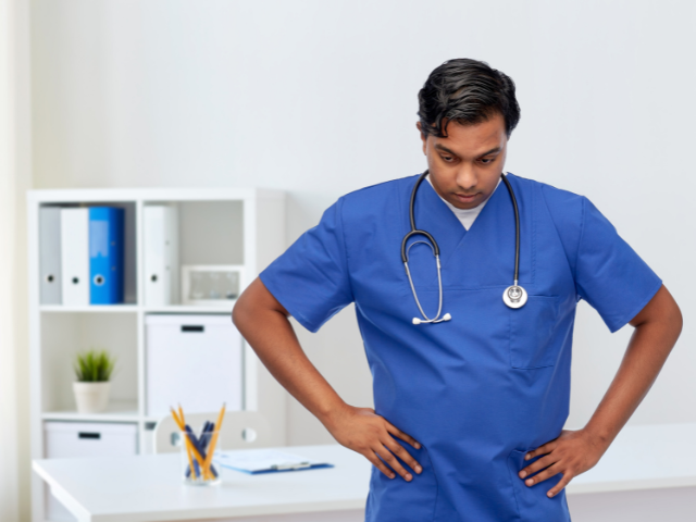 A nurse looks downward with his hands on his hips.